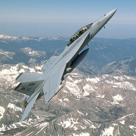 F/A-18F Super Hornet at high angle of attack over a snowy mountain range.